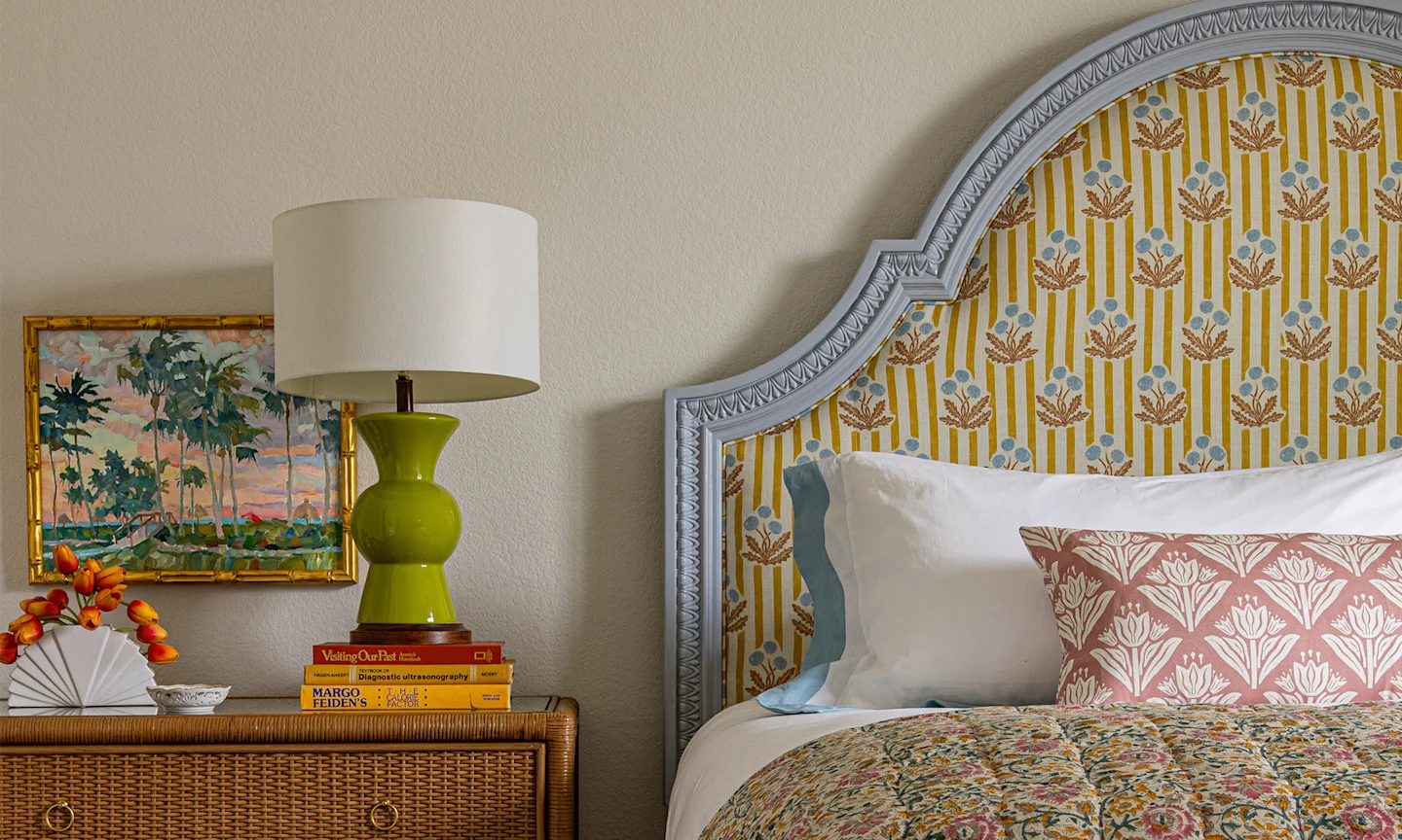 Bedroom with a headboard upholstered with a yellow and blue striped floral block print fabric.