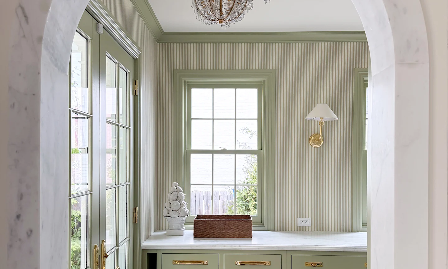 Kitchen with green vertical stripe wallpaper, green cabinetry and trim around windows and brass accents.