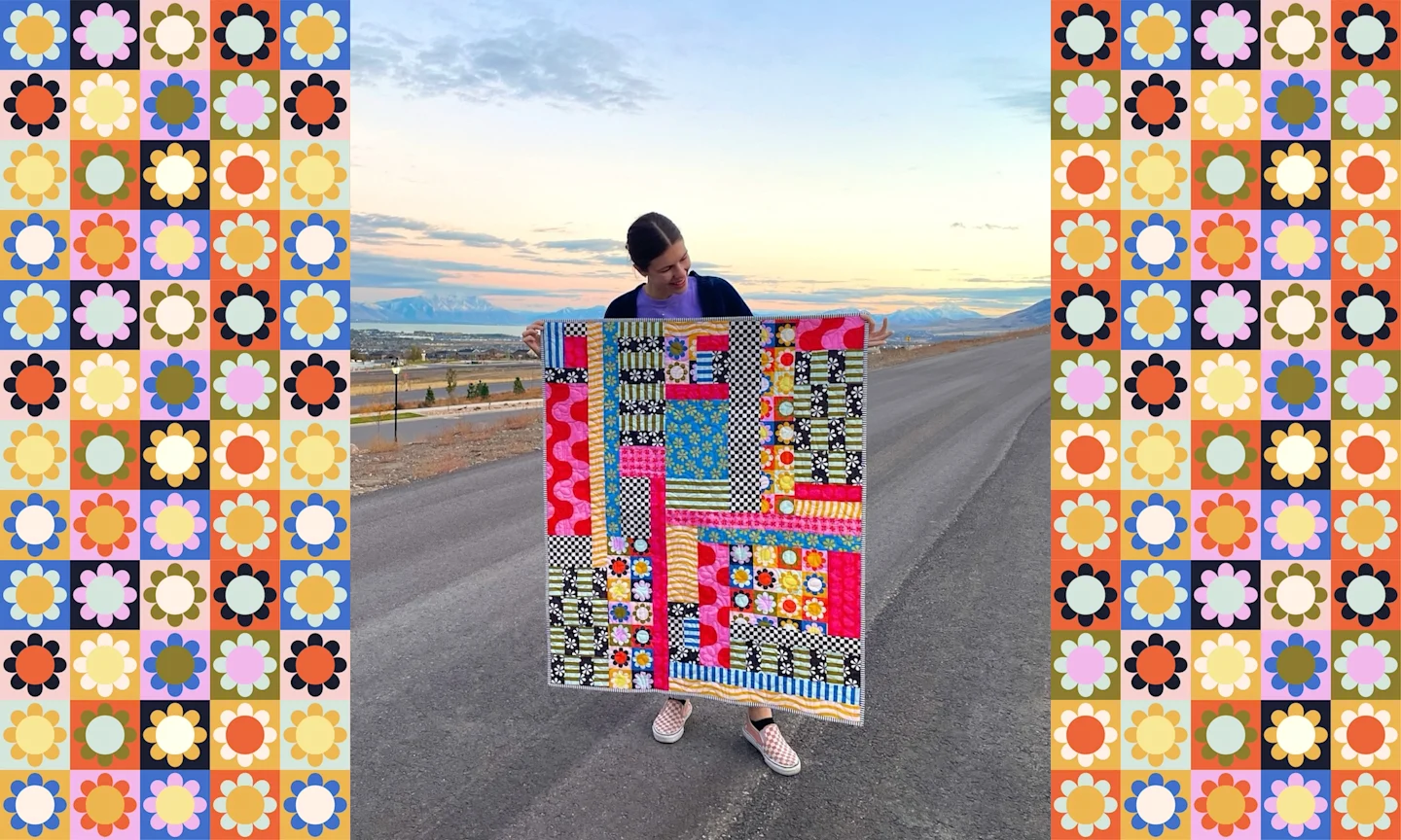 a woman standing in the middle of a road in the desert. She is holding a colorful quilt up in front of her body. 