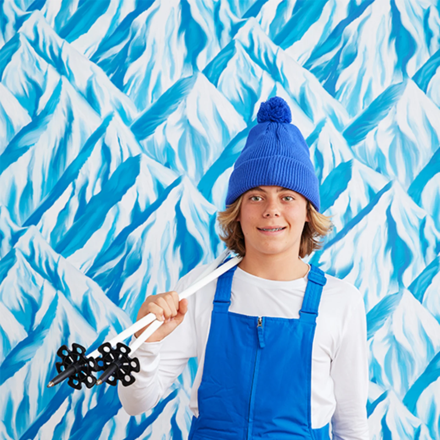 Boy in ski gear next to blue mountain wallpaper.
