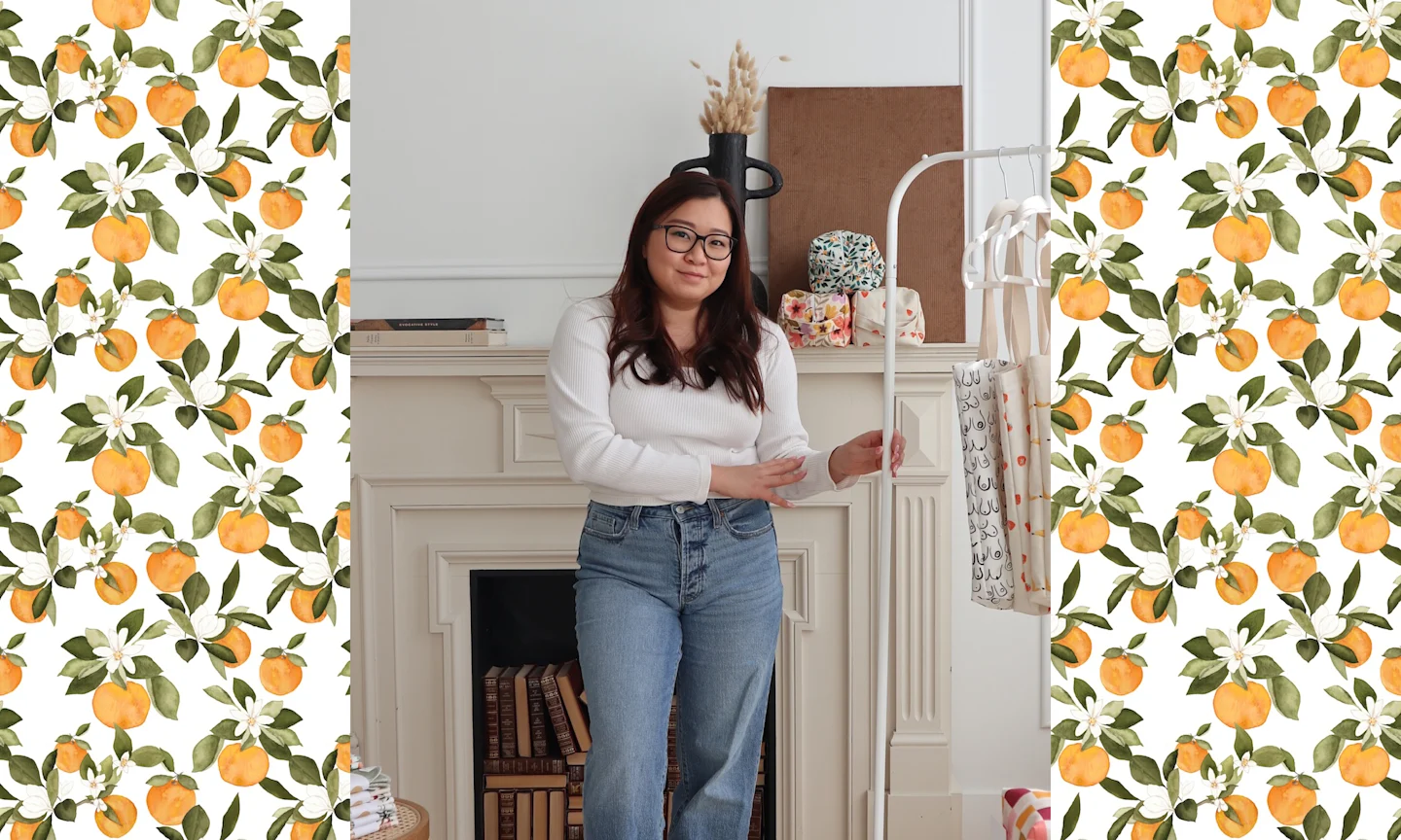 a woman in jeans and a white shirt stands in front of a fireplace. Some softgoods and accessories are displayed around her.