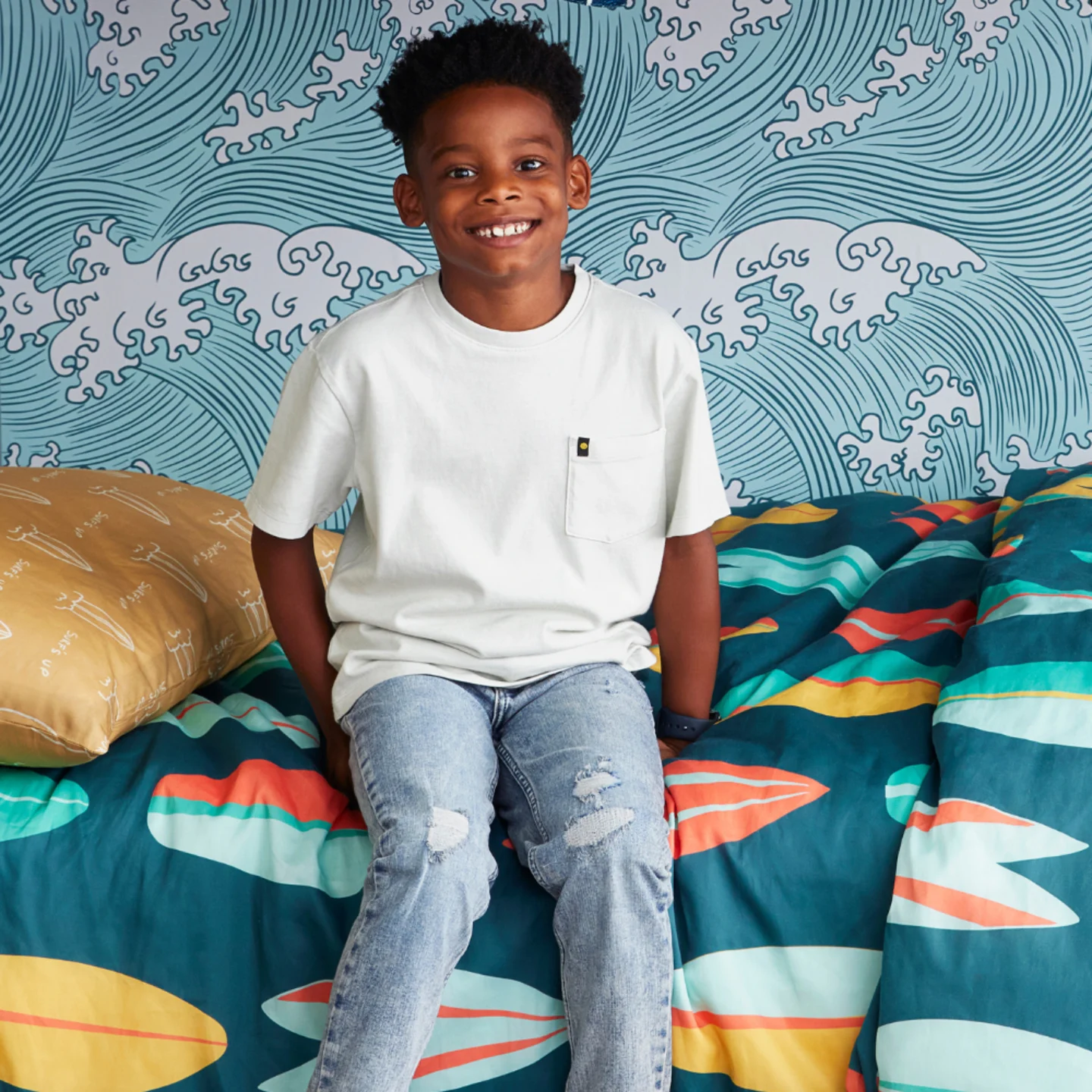 Boy in bunk bed with surf themed wallpaper and bedding.